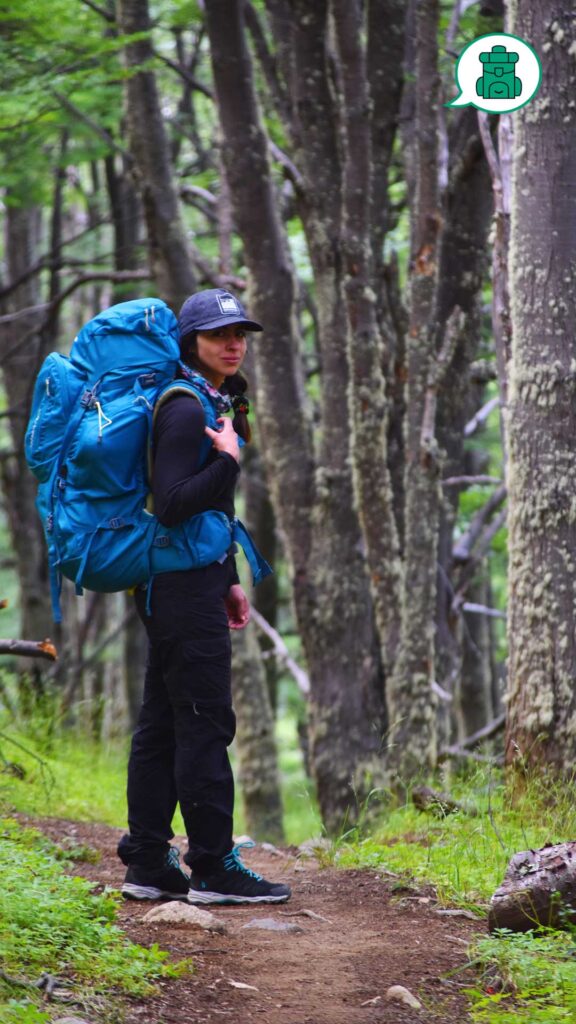 Mujer caminando con mochila en un bosque frondoso.