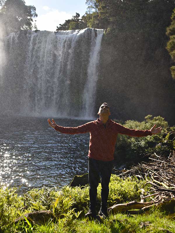 Gratitud en la naturaleza Viajero agradeciendo frente a una cascada en el bosque de Kerikeri.