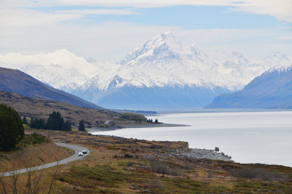 Rumbo a Mount Cook, la montaña más alta de Nueva Zelanda Carretera solitaria, lago azul y Mount Cook en el horizonte.
