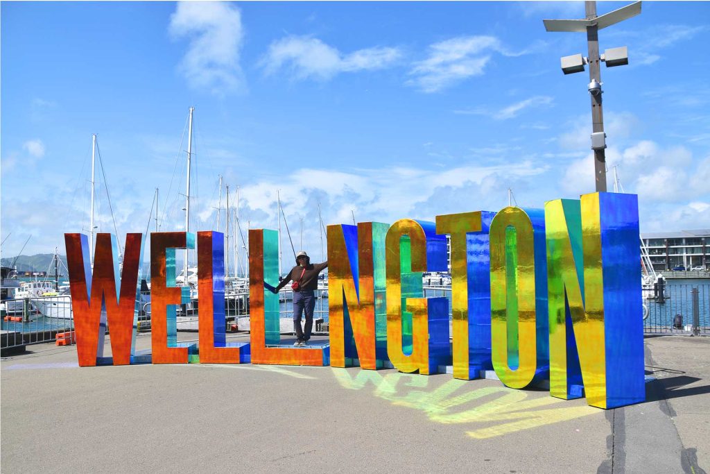 Bienvenida a Wellington, capital del viento Mujer posando frente al letrero gigante de Wellington.