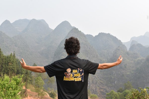 Aventura y solidaridad en Ha Giang. John con camiseta de Ha Giang Tour y montañas de fondo en Vietnam.