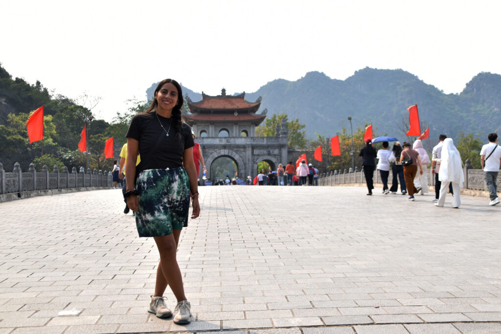 Camila posando en una amplia plaza frente a una puerta tradicional con banderas rojas en Ninh Binh.