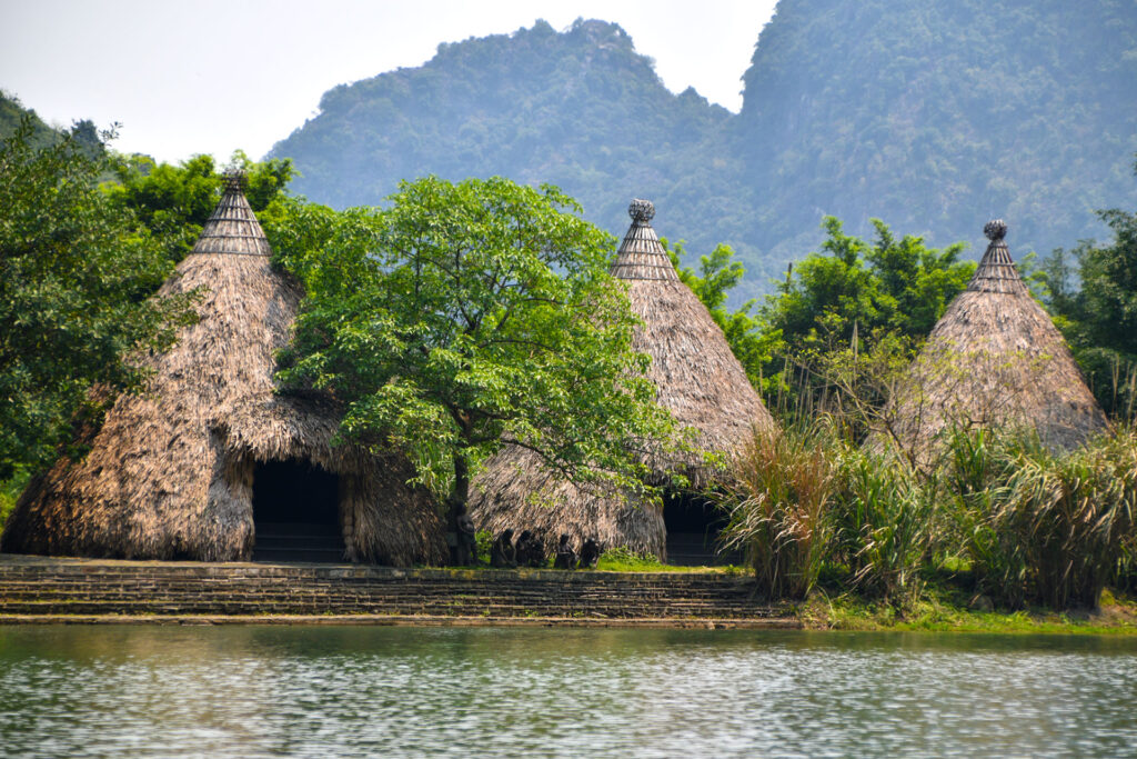 Estructuras con techos de paja de estilo tradicional situadas frente a un lago tranquilo durante la Ruta en Ninh Binh Vietnam.