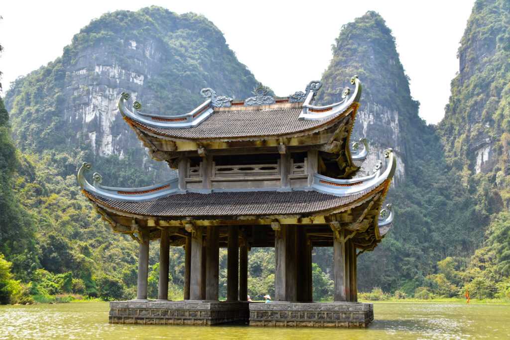 Pagoda de madera de estilo antiguo situada sobre el agua rodeada de montañas verdes.