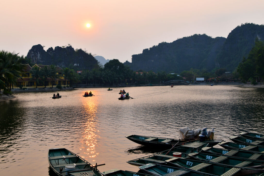 El sol ocultándose tras las siluetas de las montañas kársticas reflejado en las aguas del río en Ninh Binh.