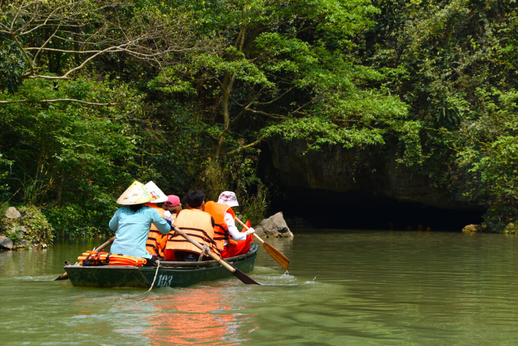 Bote de remos navegando cerca de la entrada de una cueva kárstica en la Ruta en Ninh Binh Vietnam.