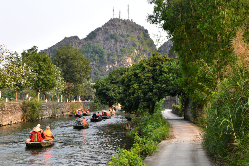 Grupo de turistas caminando por un sendero sombreado junto al río en la Ruta en Ninh Binh Vietnam.