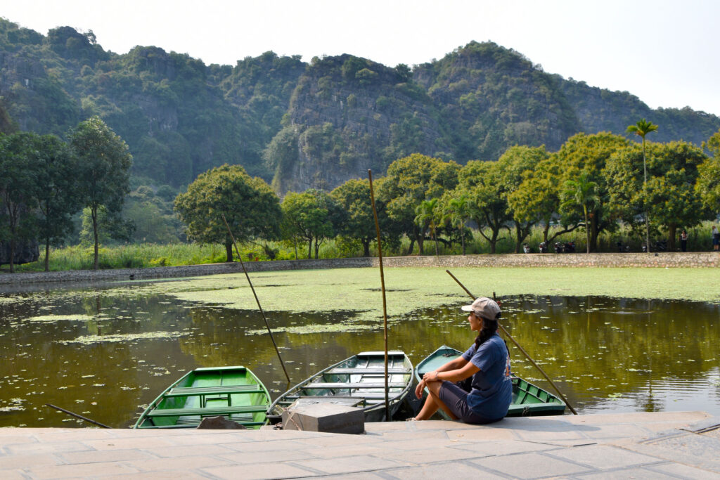Viajera descansando frente a un lago rodeado de densa vegetación durante la Ruta en Ninh Binh Vietnam con Parche Y Le Cuento.