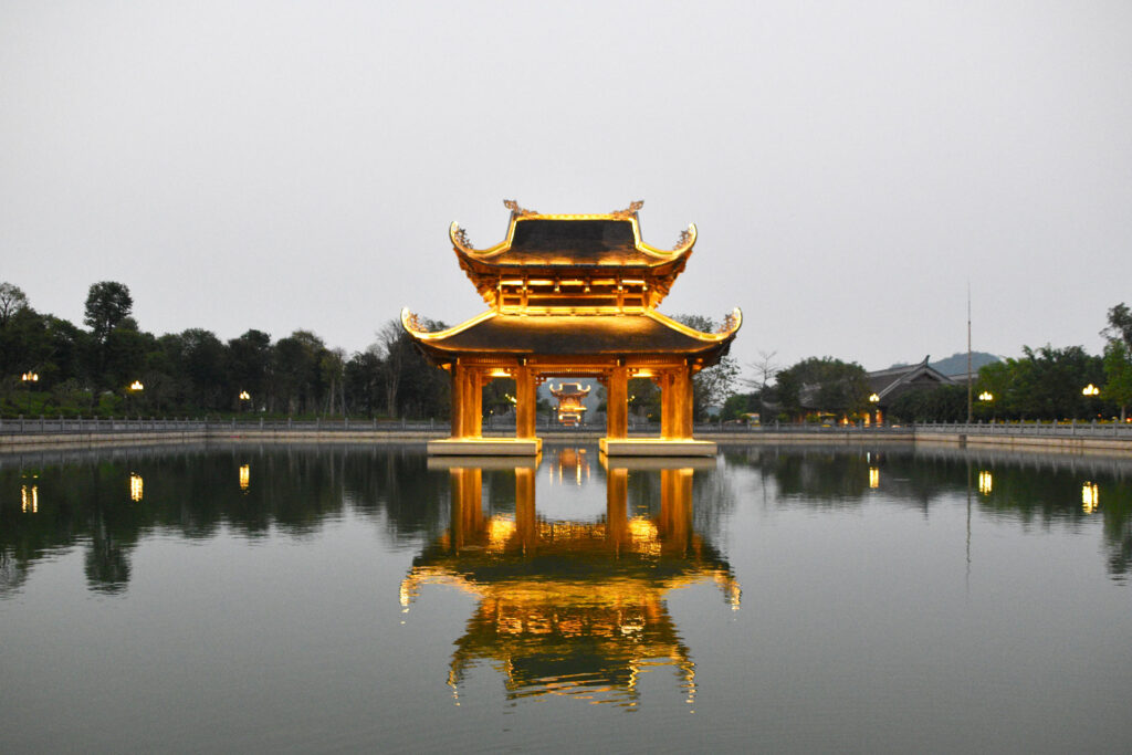 Majestuosa pagoda iluminada reflejada simétricamente en el agua durante la Ruta en Ninh Binh Vietnam.