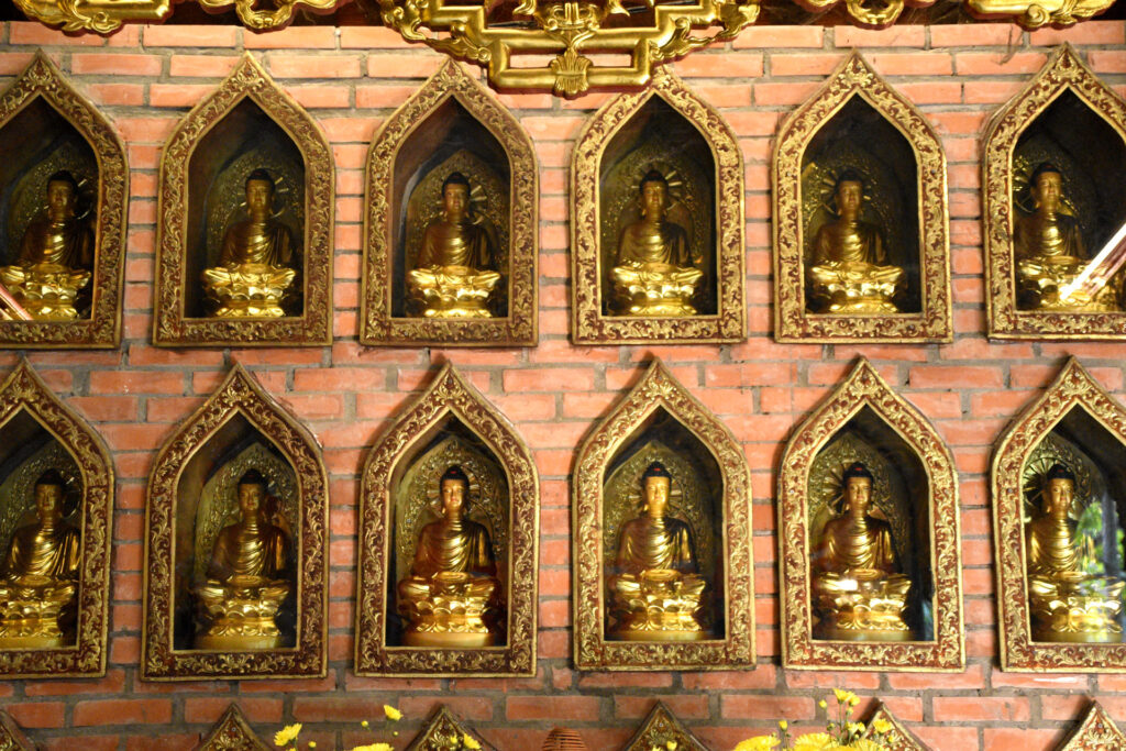 Pared con nichos que contienen pequeñas estatuas doradas de Buda en un templo de Ninh Binh.