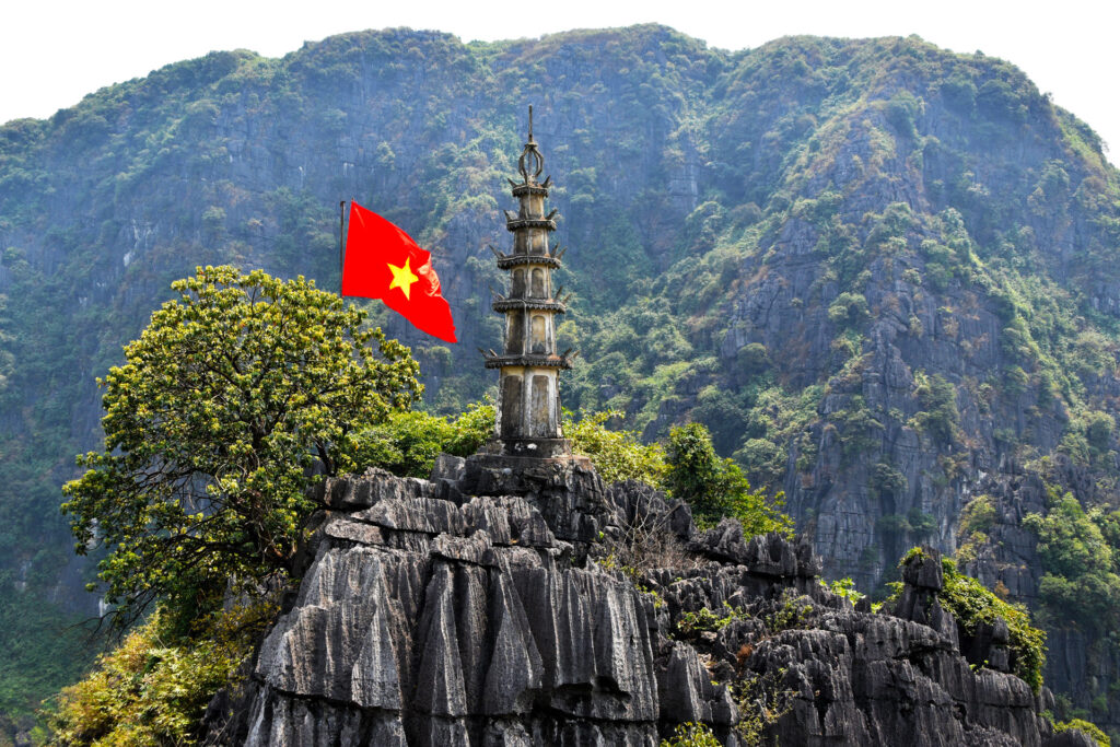 Una pequeña pagoda coronando la cima de una montaña bajo la bandera nacional de Vietnam.