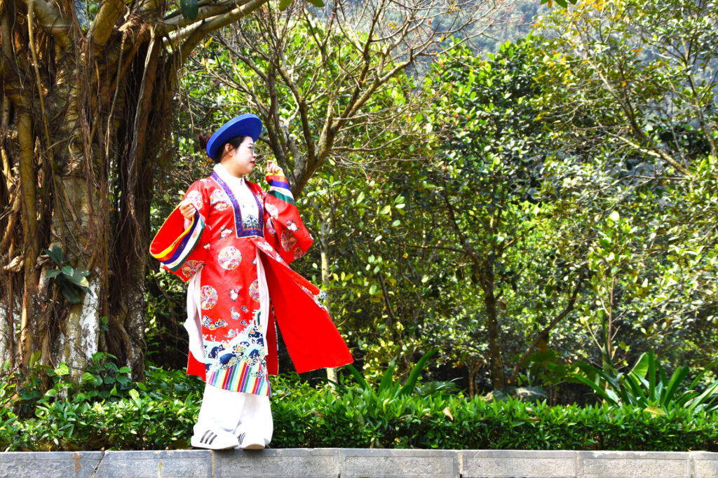Artista local con traje tradicional rojo realizando una presentación en un entorno natural de Vietnam.