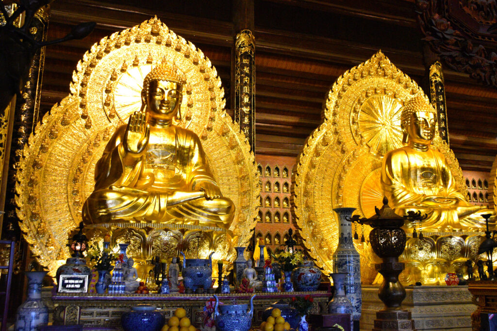 Dos imponentes estatuas doradas de Buda sentadas en un altar decorado durante la Ruta en Ninh Binh Vietnam.