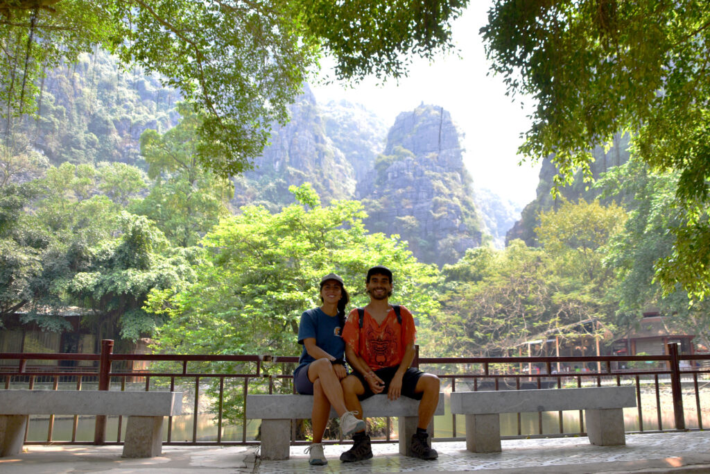 Pareja sentada en un banco de piedra bajo grandes árboles frente a las montañas de Vietnam.