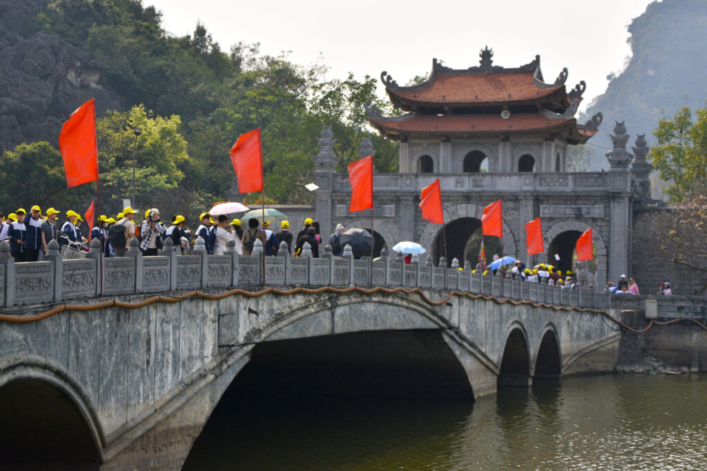 Puente de piedra arqueado decorado con banderas rojas sobre un río en Ninh Binh.