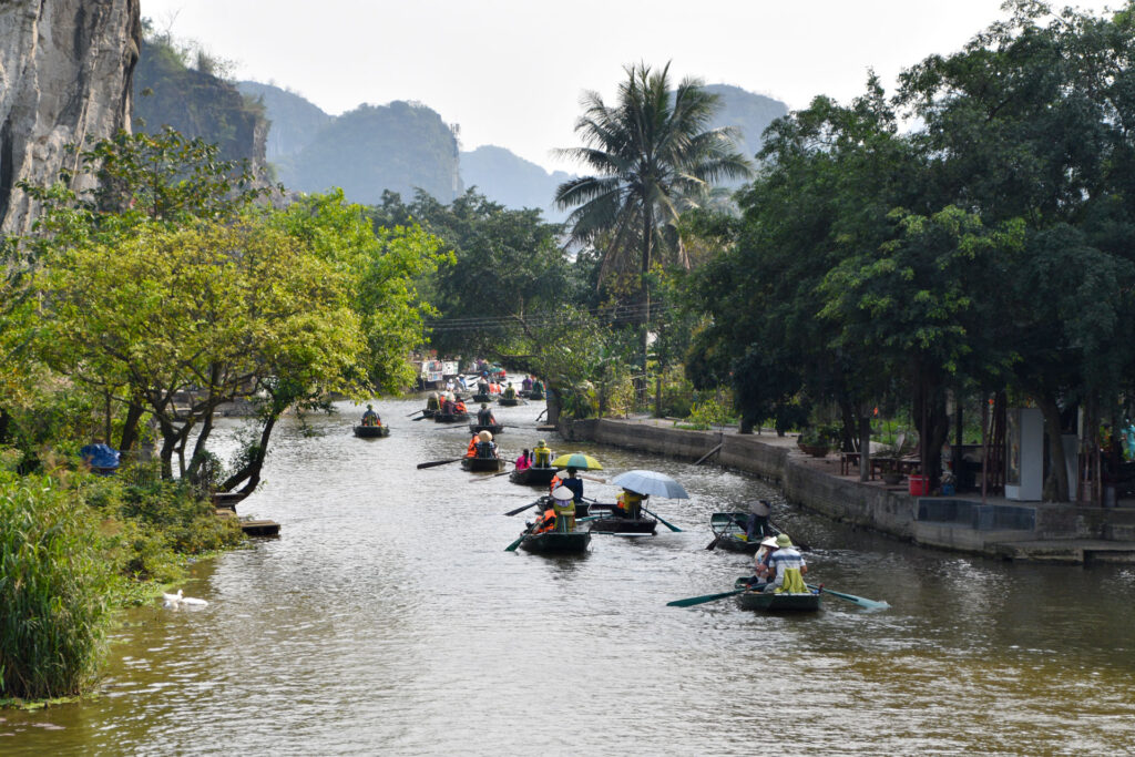 Fila de botes de remos avanzando por un canal estrecho entre colinas verdes en Ninh Binh.